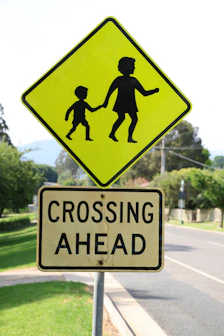 A yellow crossing sign sitting on the side of a road