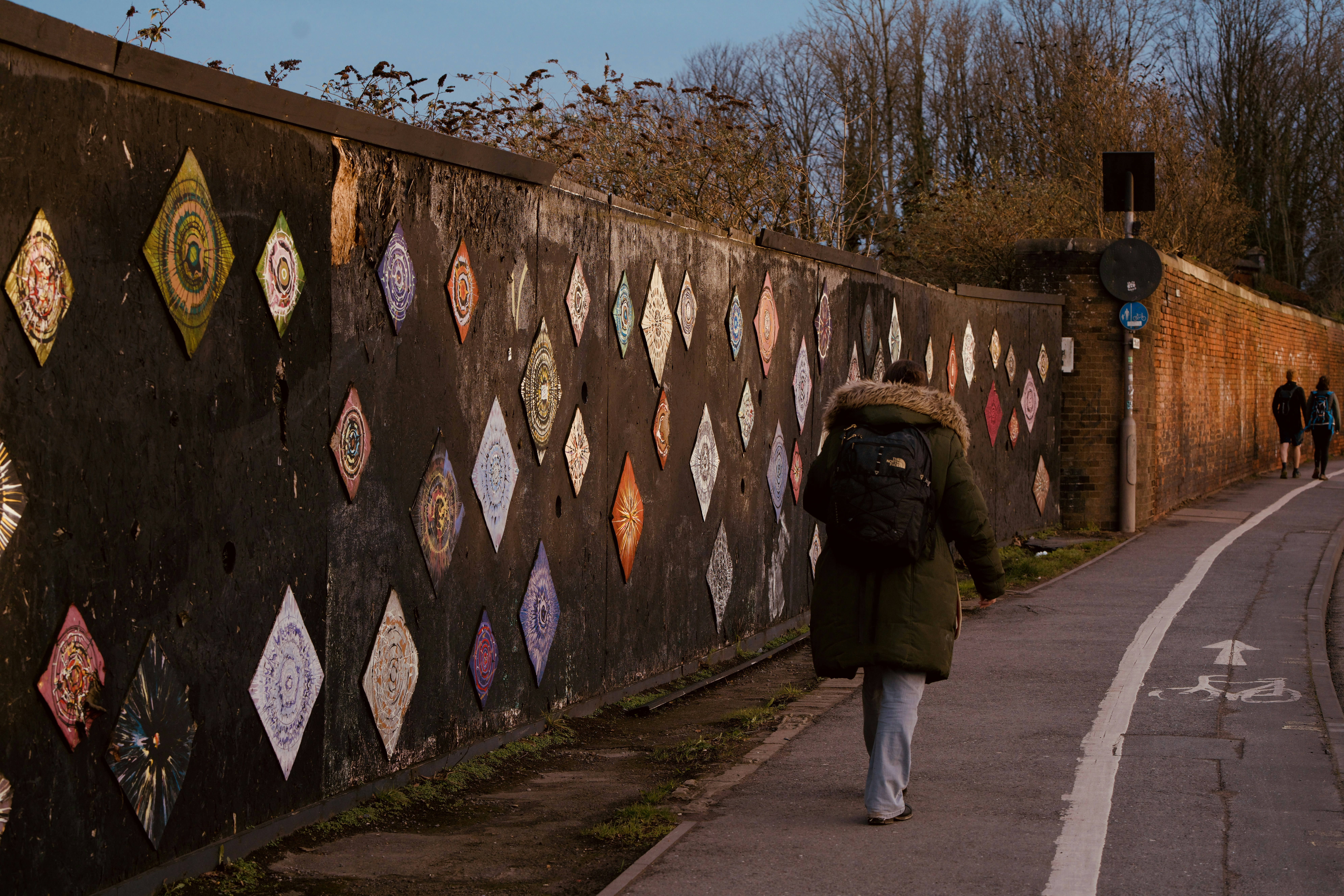 A woman walking down a sidewalk next to a wall