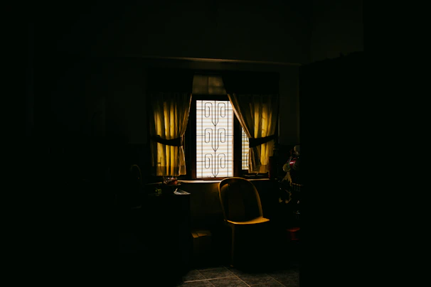 A dark room with a chair and a window