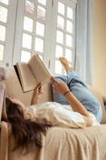 A woman laying on a couch reading a book