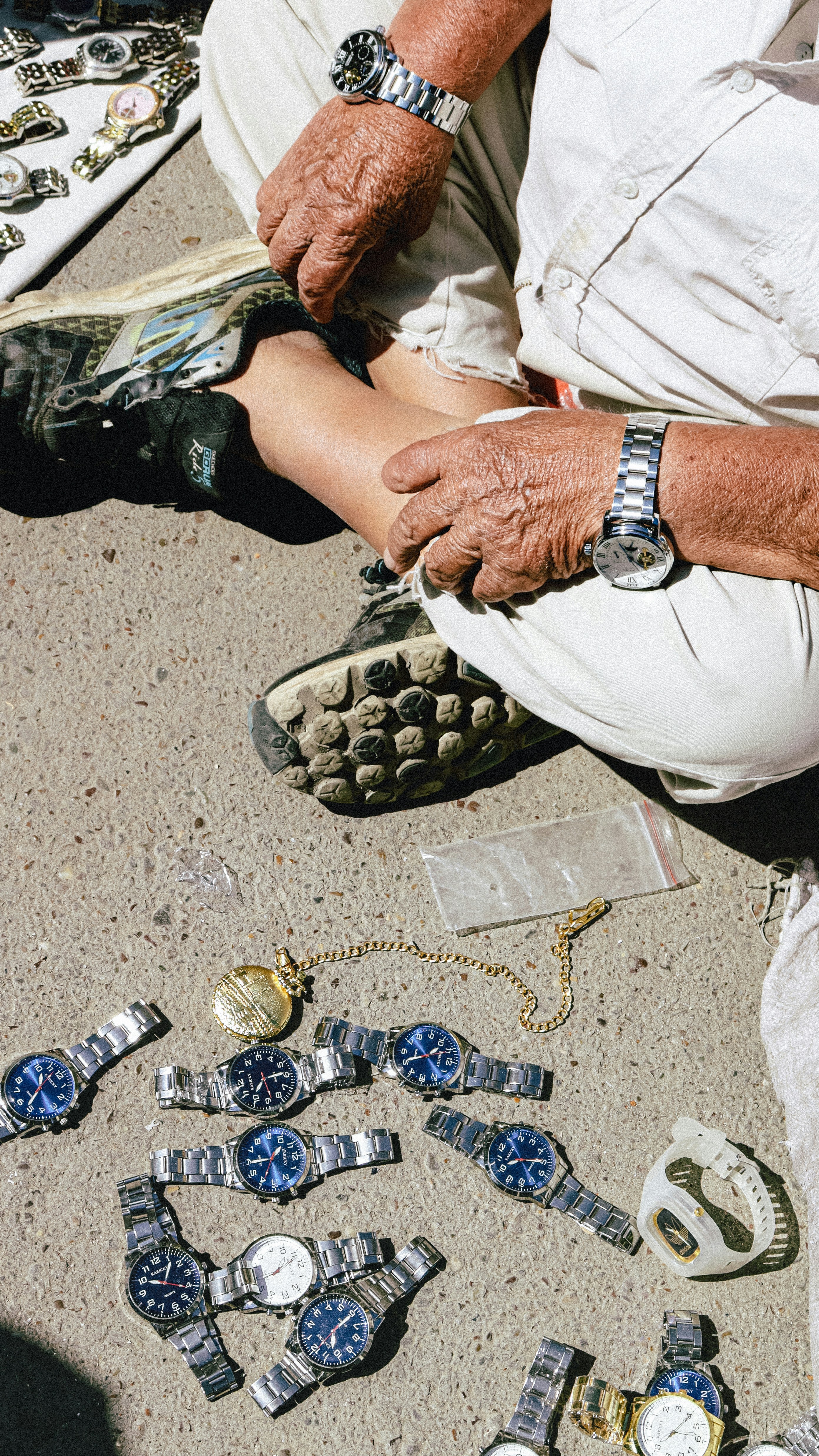 A man sitting on the ground next to a bunch of bracelets