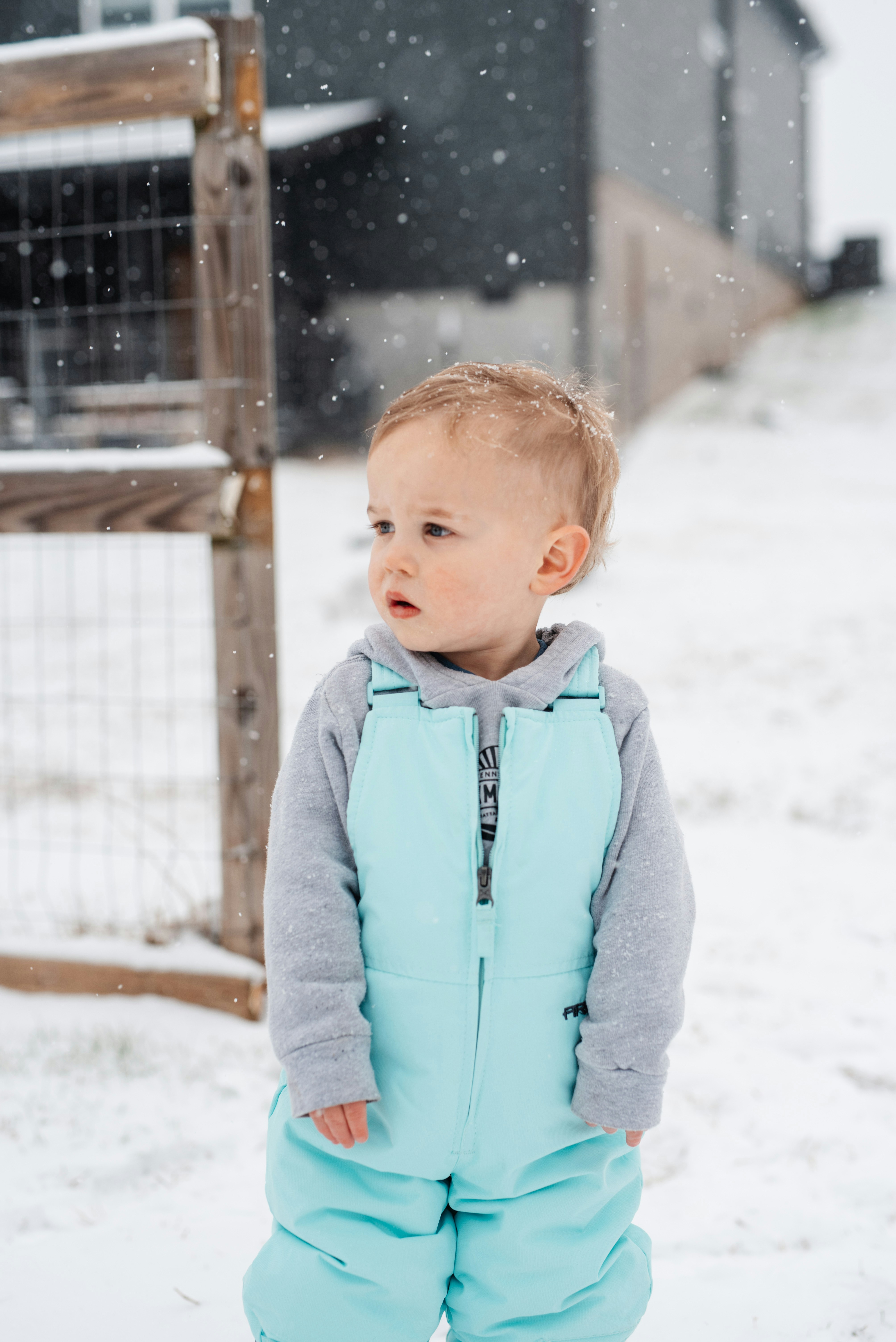 A toddler standing in the snow wearing a blue snowsuit