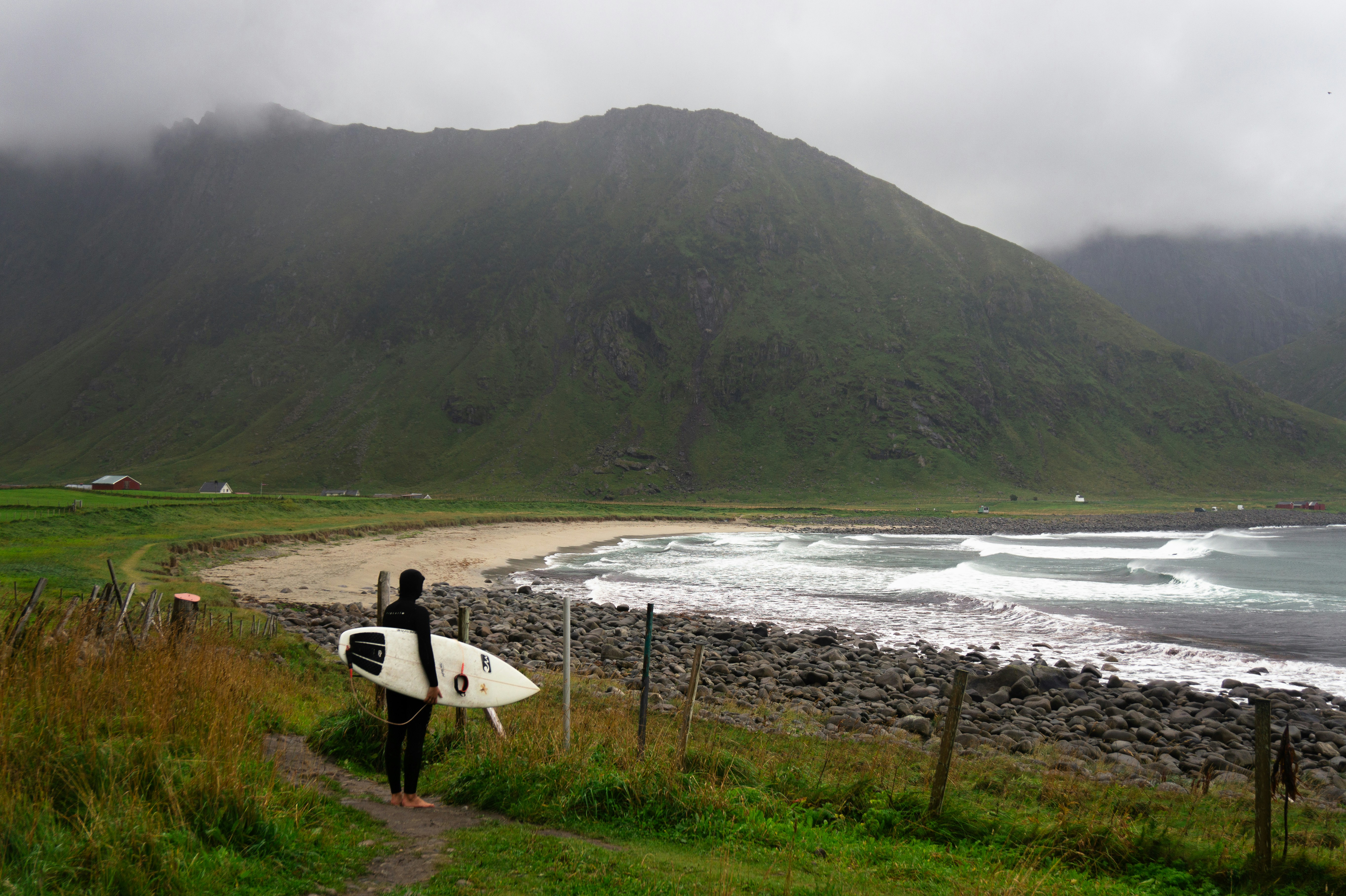 A man holding a surfboard on top of a lush green hillside
