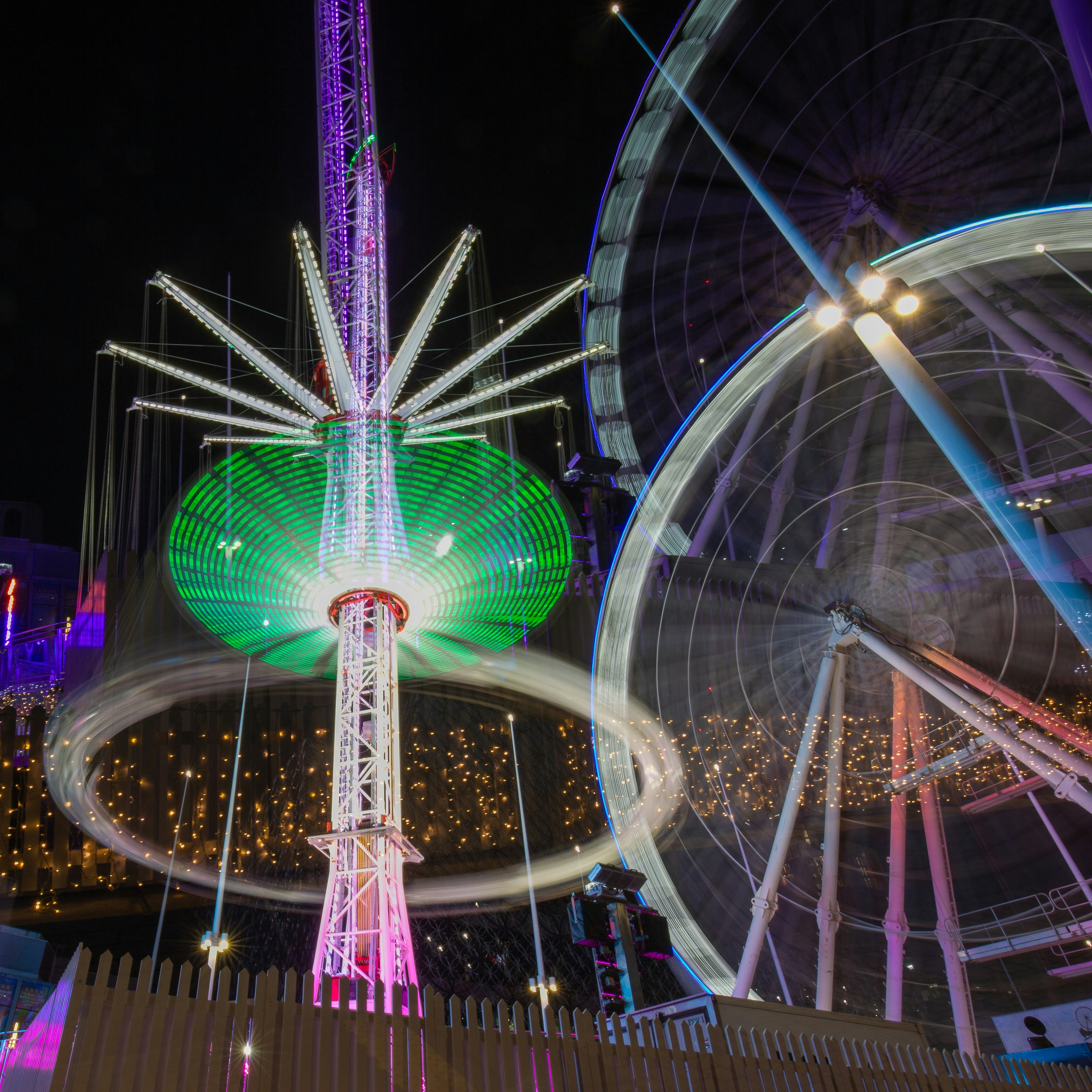 A ferris wheel lit up at night with a ferris wheel in the background