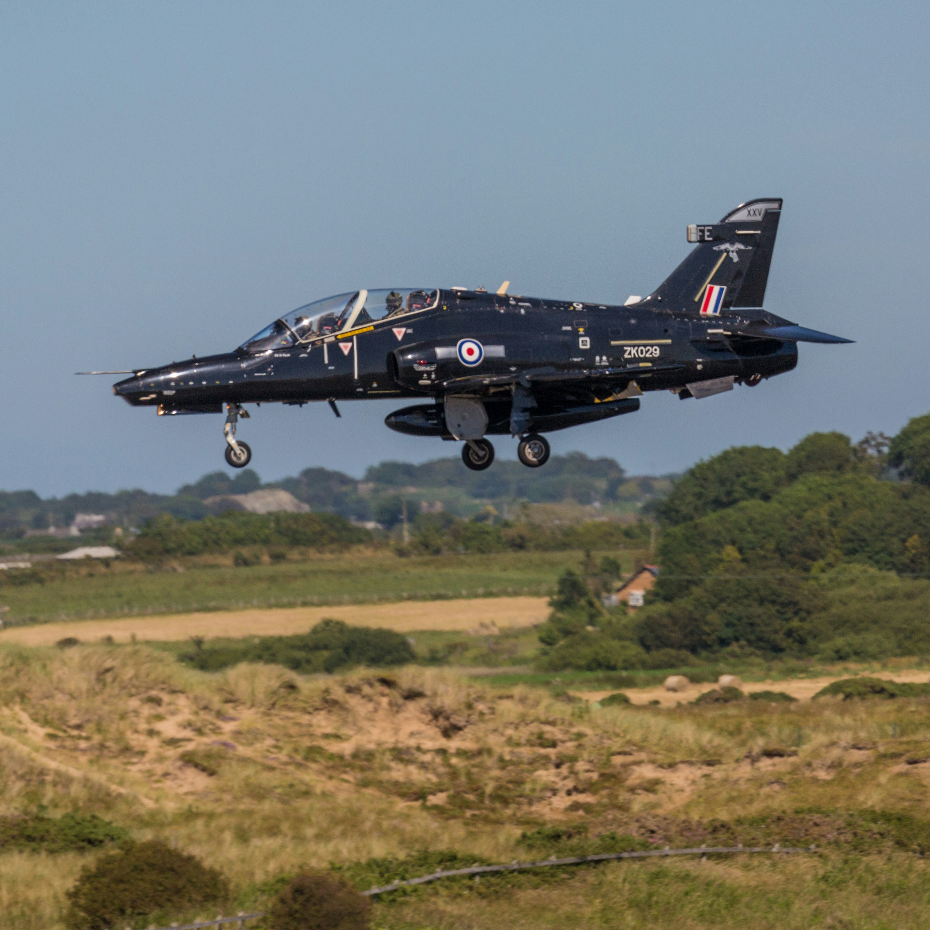A fighter jet flying over a lush green field