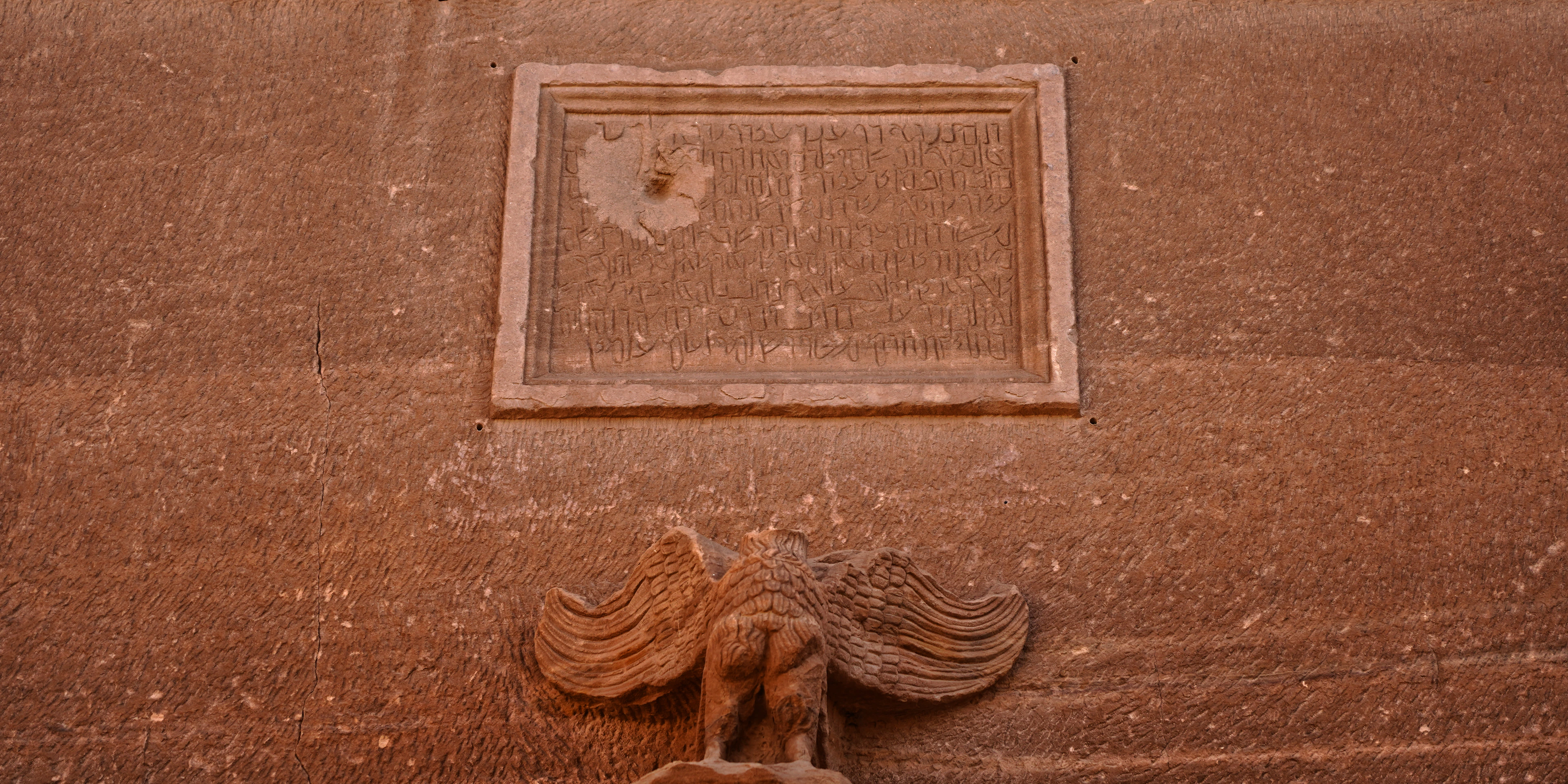 Close-up of a carved eagle relief above a niche on a sandstone Nabataean tomb facade.