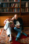 A man and woman sitting on a rug in front of a bookshelf