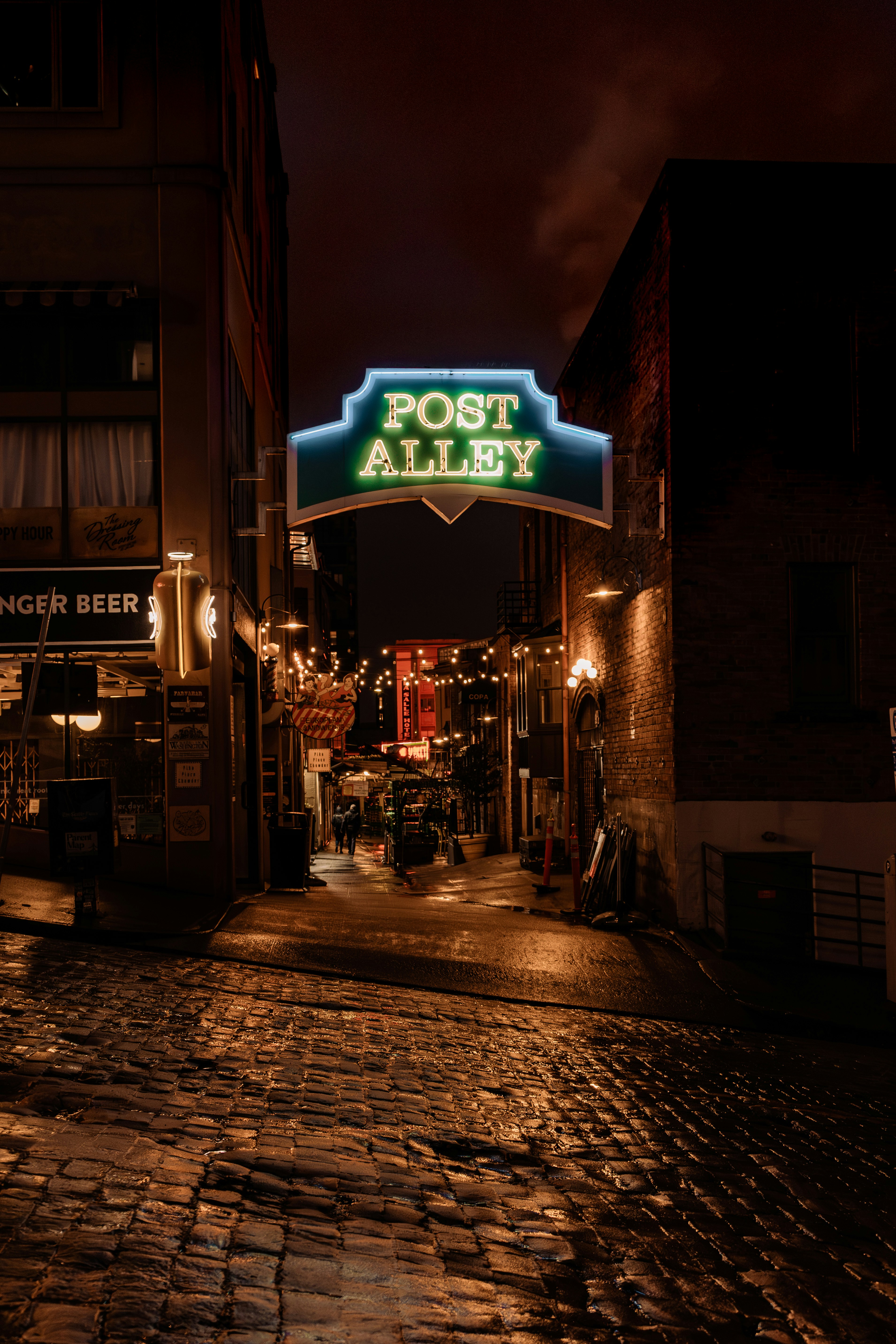 A cobblestone street with a post alley sign lit up at night
