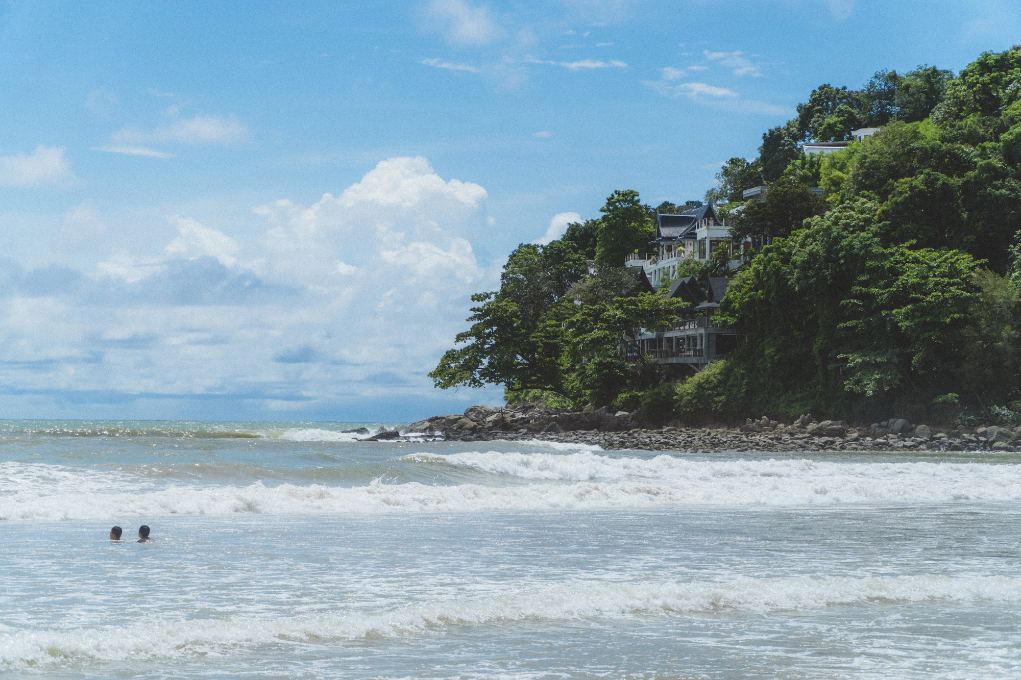 Waves at Kamala Beach below a wooded headland with villas