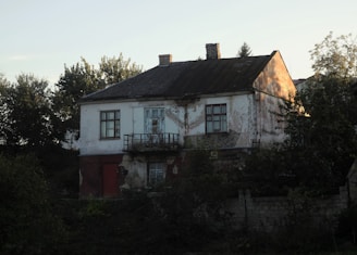 A large white house sitting next to a forest
