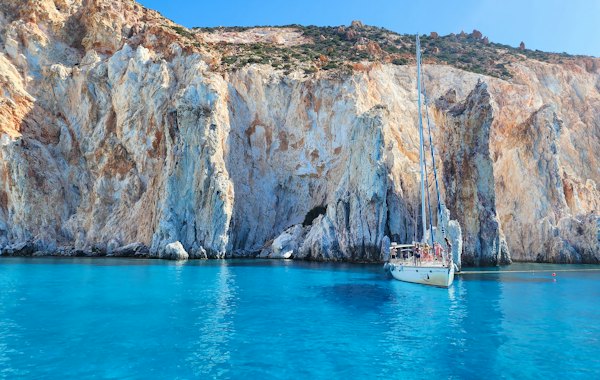 A boat floating in a body of water next to a mountain — Milos, Greece