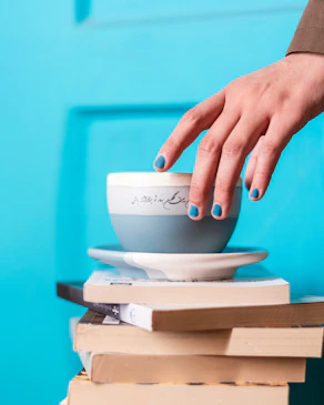 A woman's hand reaching for a cup on top of a stack of books