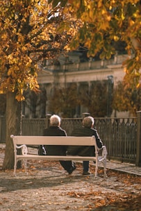 Two elderly people sitting on a bench in a park