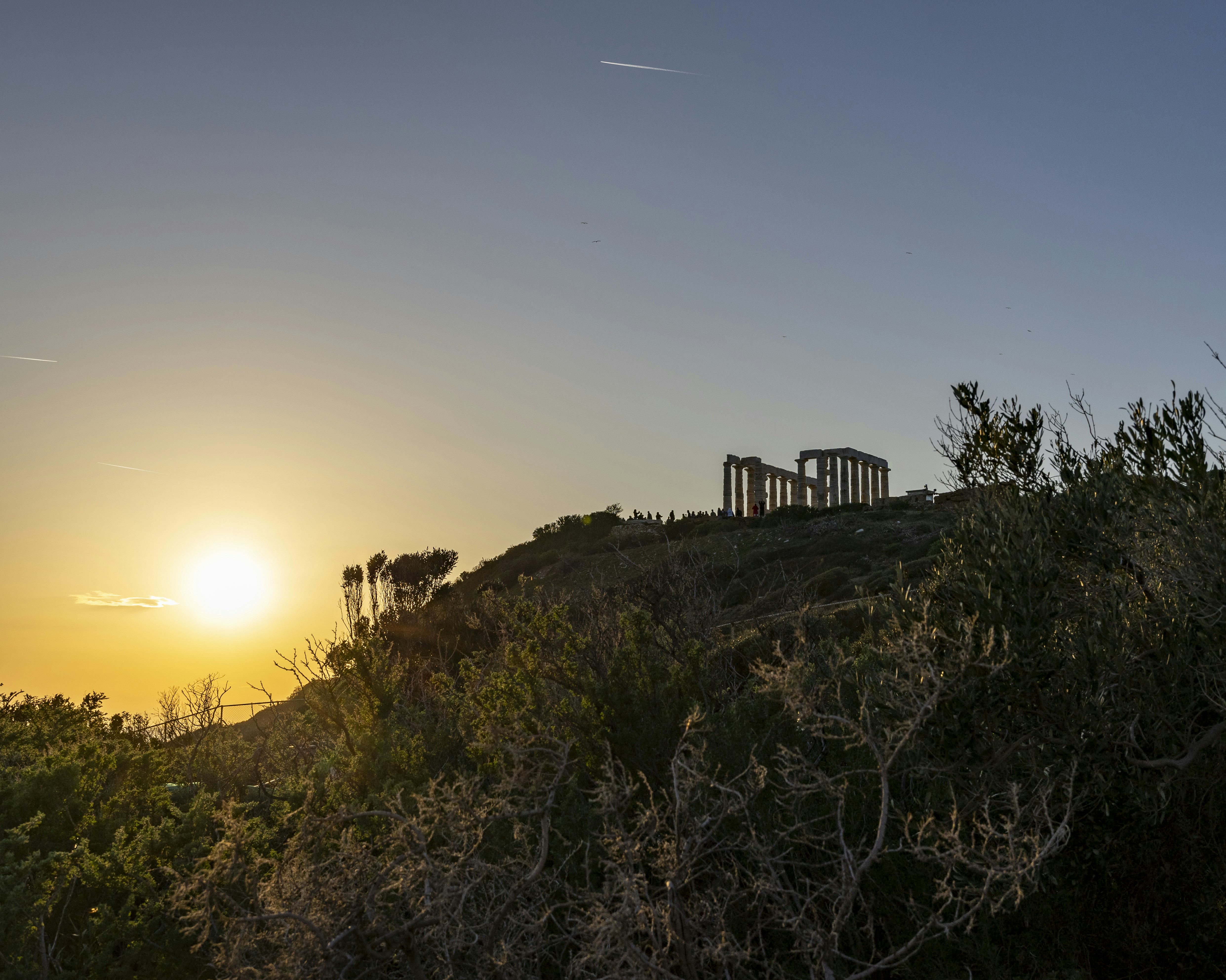 The sun is setting over a hill with trees