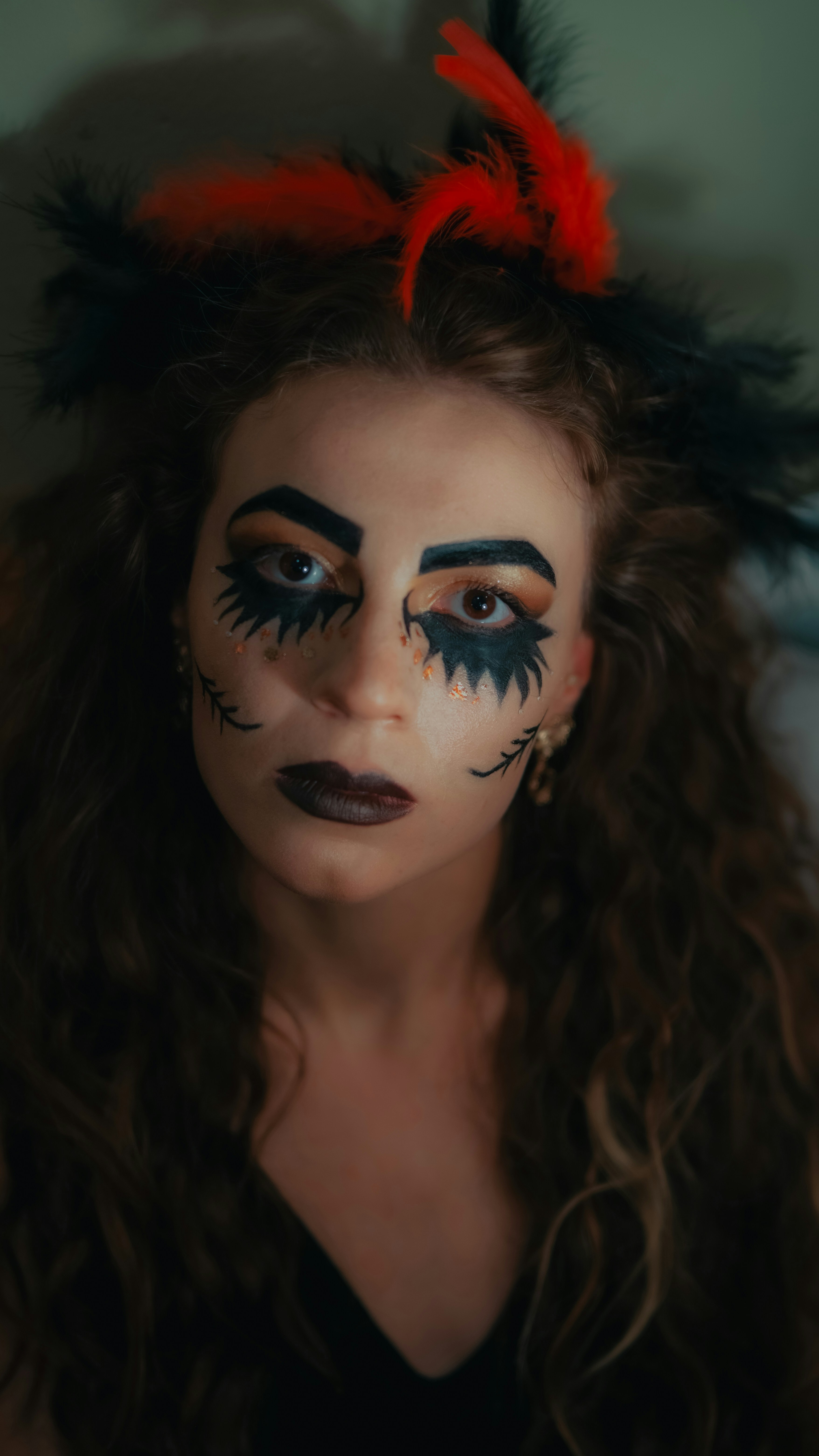 A woman with black makeup and red feathers on her head