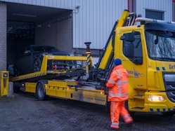 A man in an orange safety suit standing next to a yellow tow truck