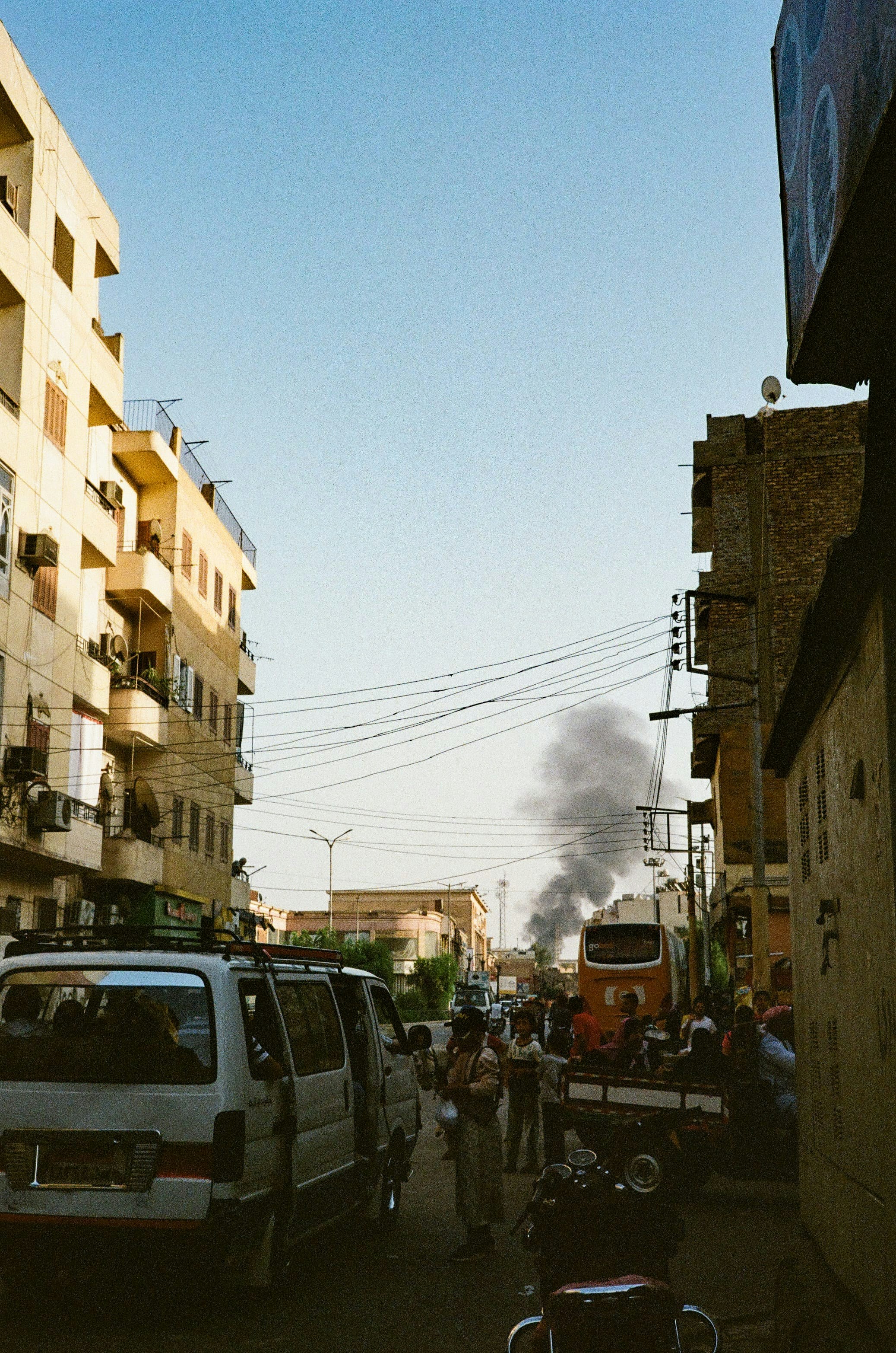 A group of people walking down a street next to parked cars