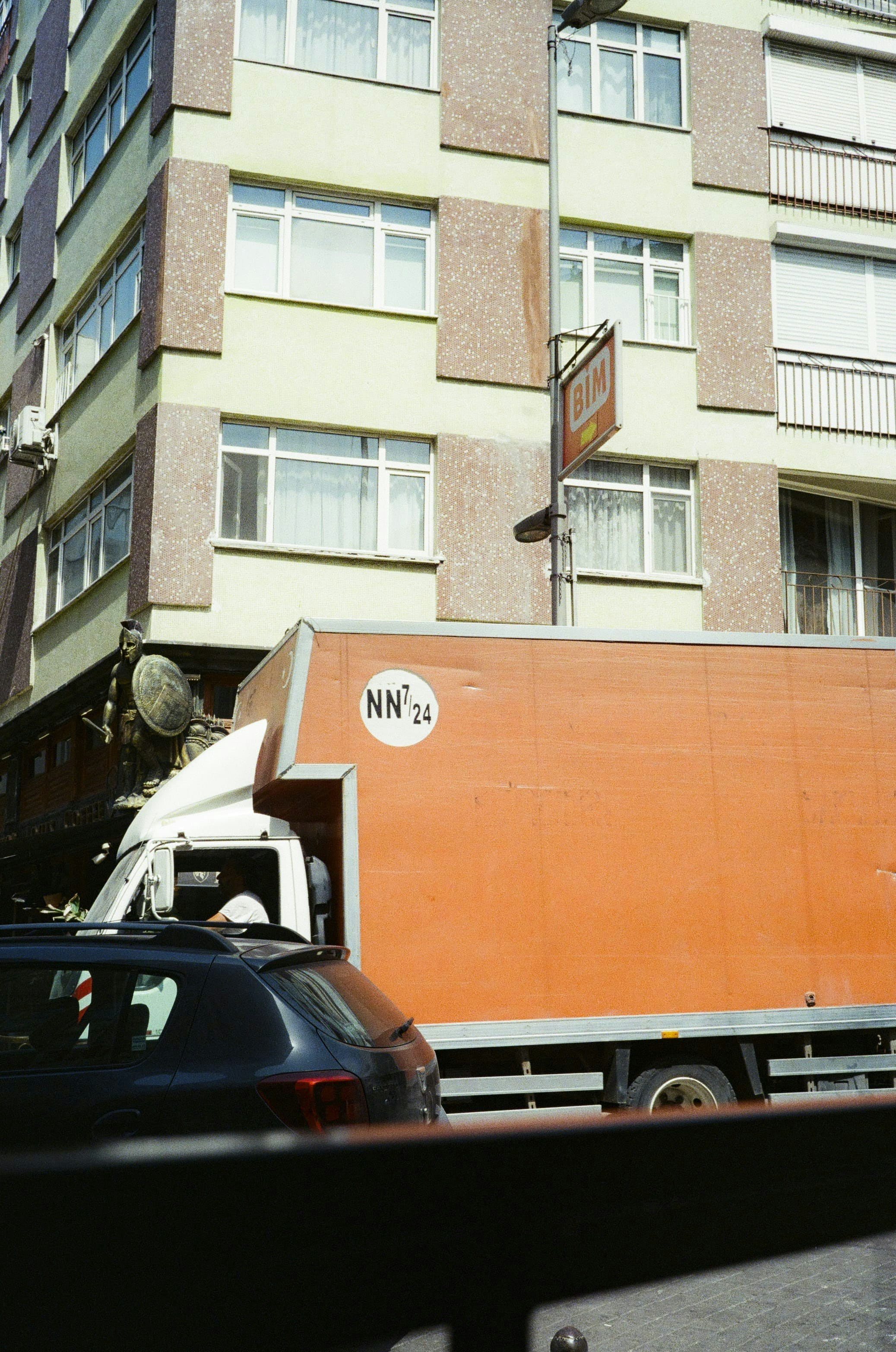 A large orange truck driving down a street next to tall buildings