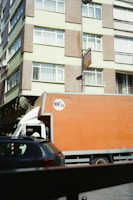A large orange truck driving down a street next to tall buildings