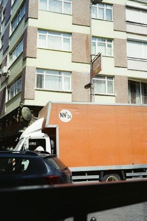 A large orange truck driving down a street next to tall buildings