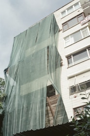 Жилищен блок, обвит в зелено защитно платно, подготвян за монтаж на външна изолация.