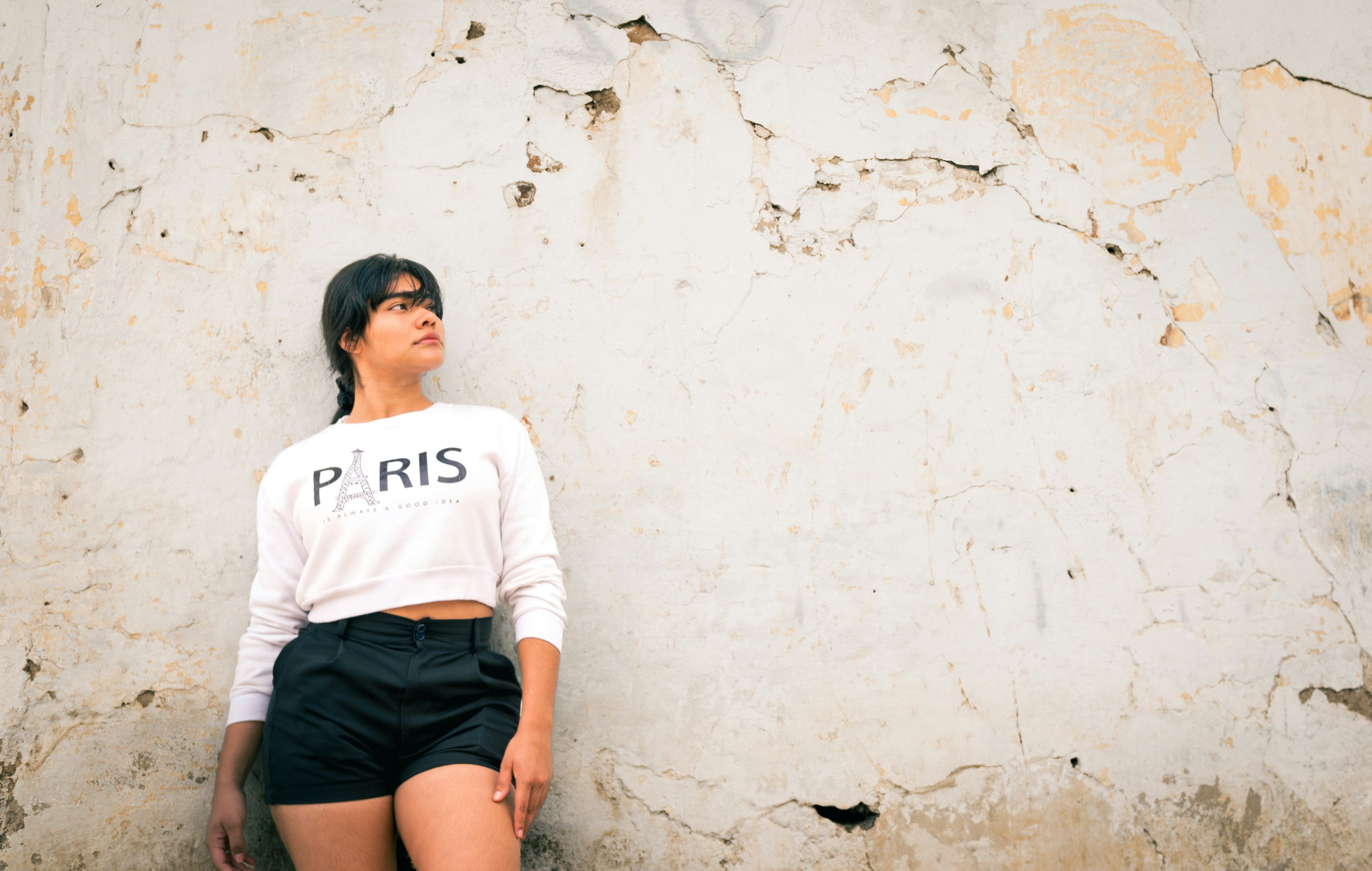 A woman leaning against a wall with her legs crossed