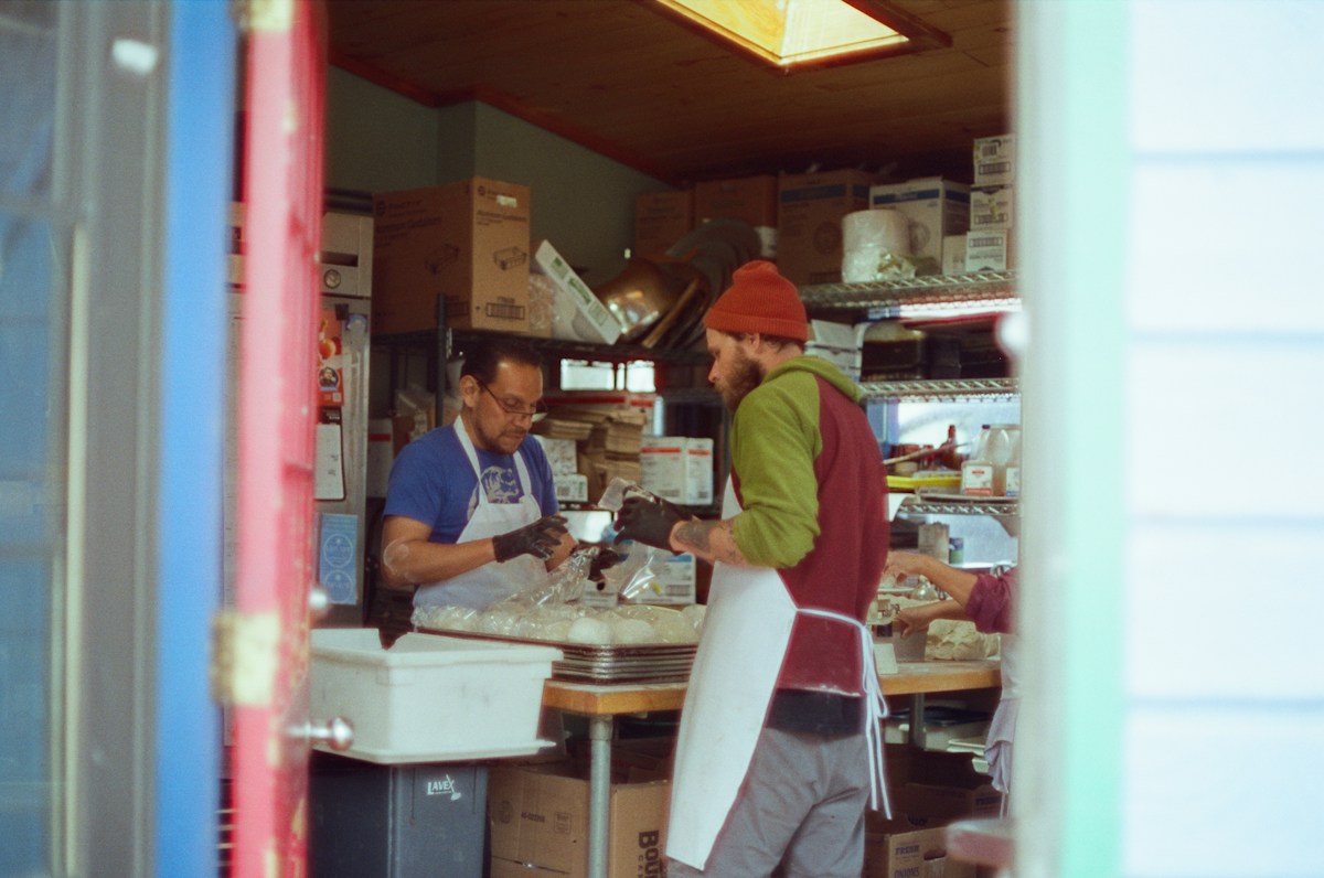 Two men stand at a store counter discussing Thanksgiving volunteer drive plans.