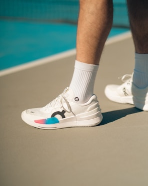 A person standing on a tennis court wearing white tennis shoes