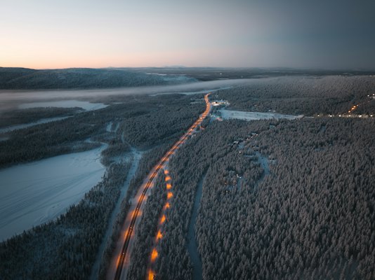 A road lit through the snowy forest at dusk, from above — Levi, Finland