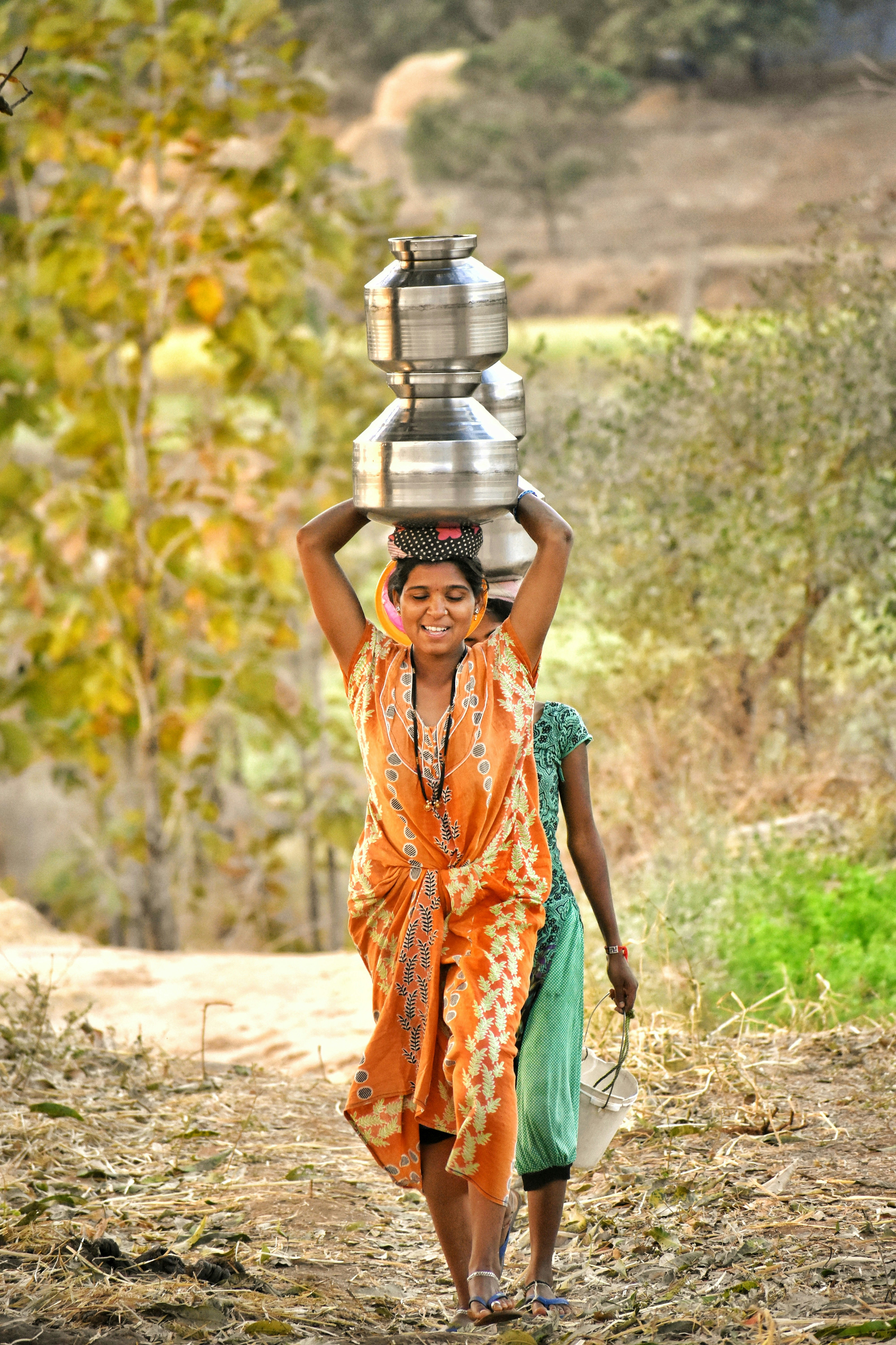 A woman carrying a pot on her head down a dirt road
