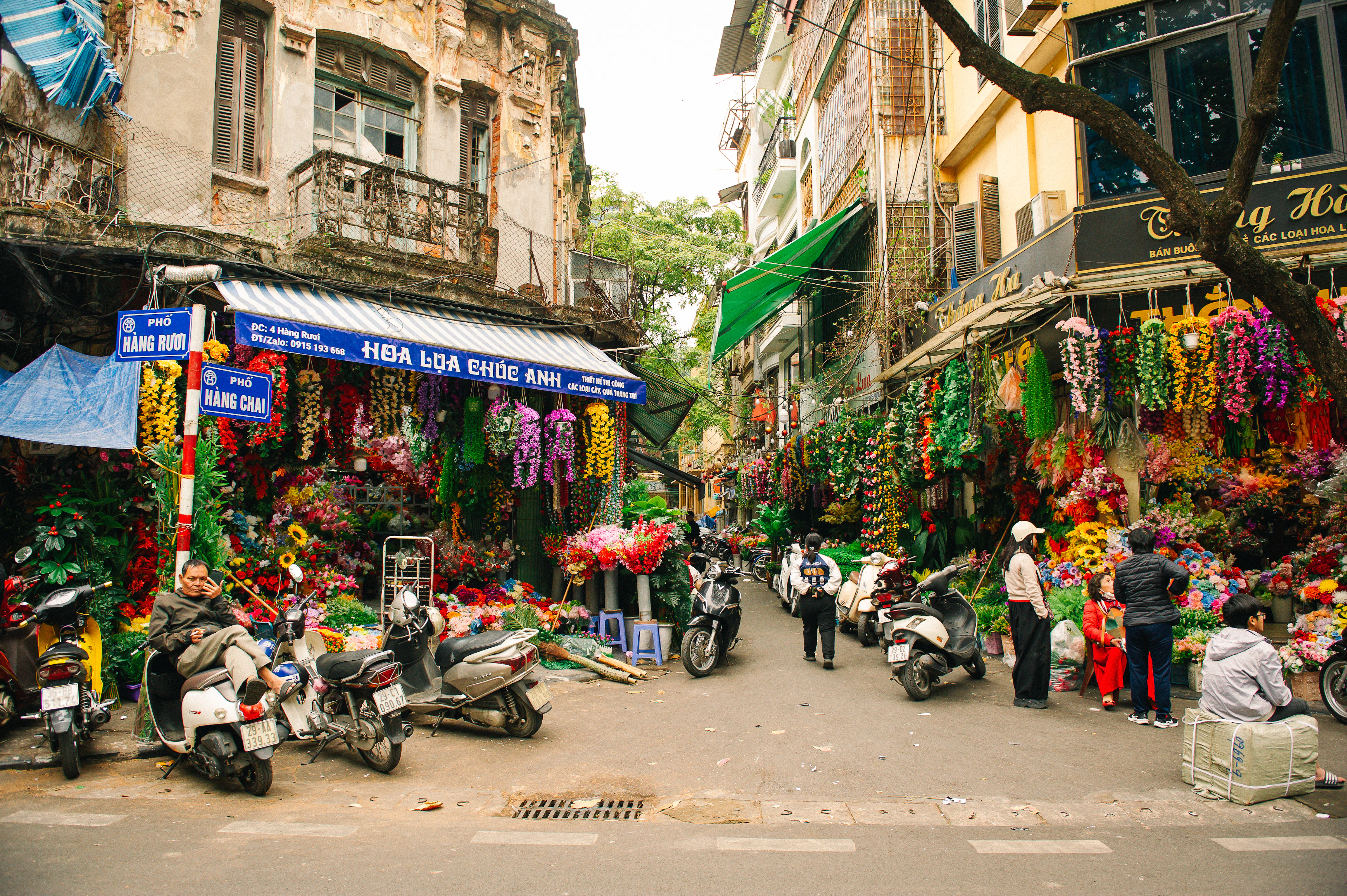 A market street in Hanoi's Old Quarter hung with garlands and paper goods, scooters parked along the kerb