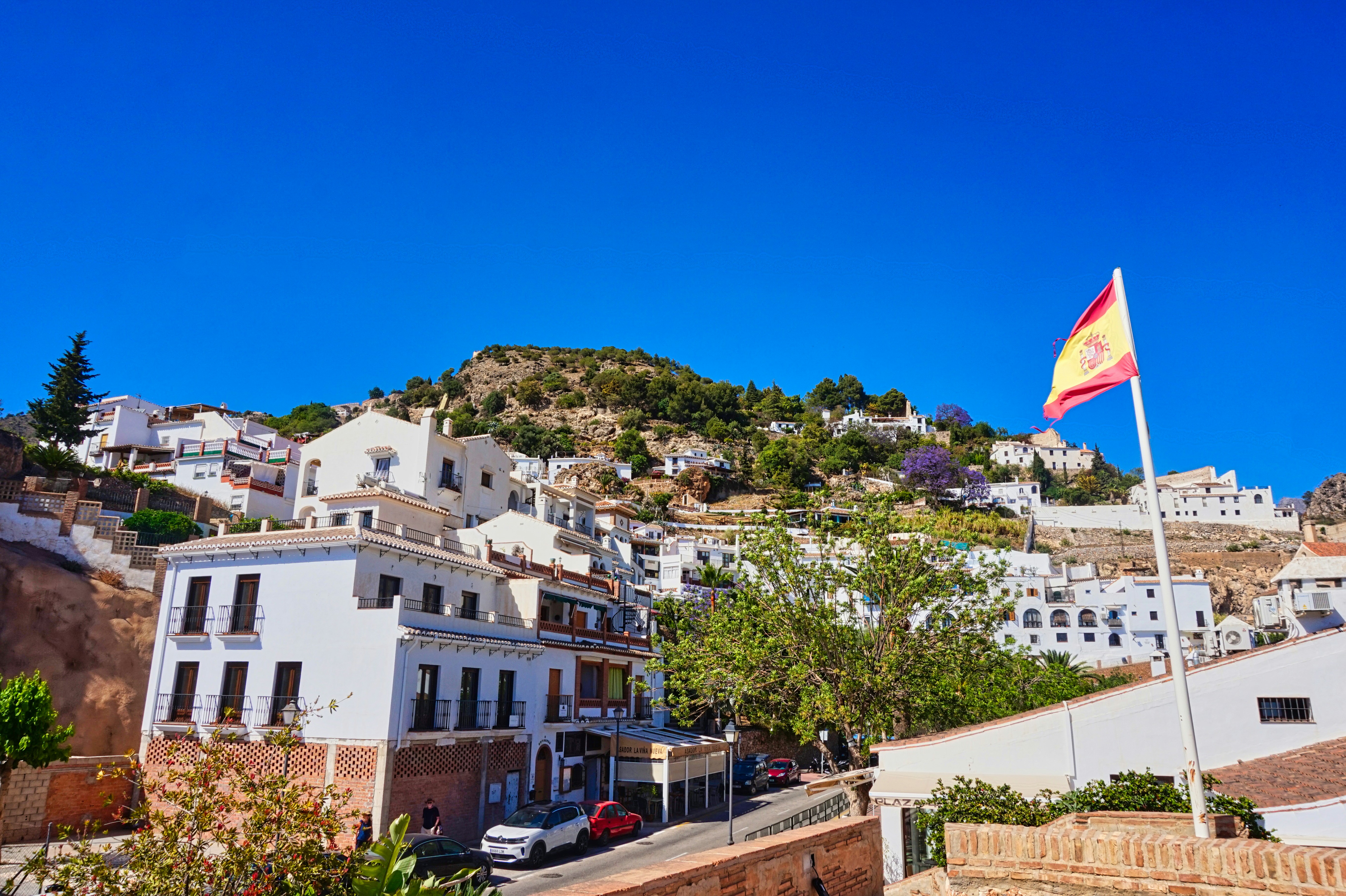 Landscape · View of Frigiliana with white houses and a mountain in the background and a flag of Spain moving in the wind