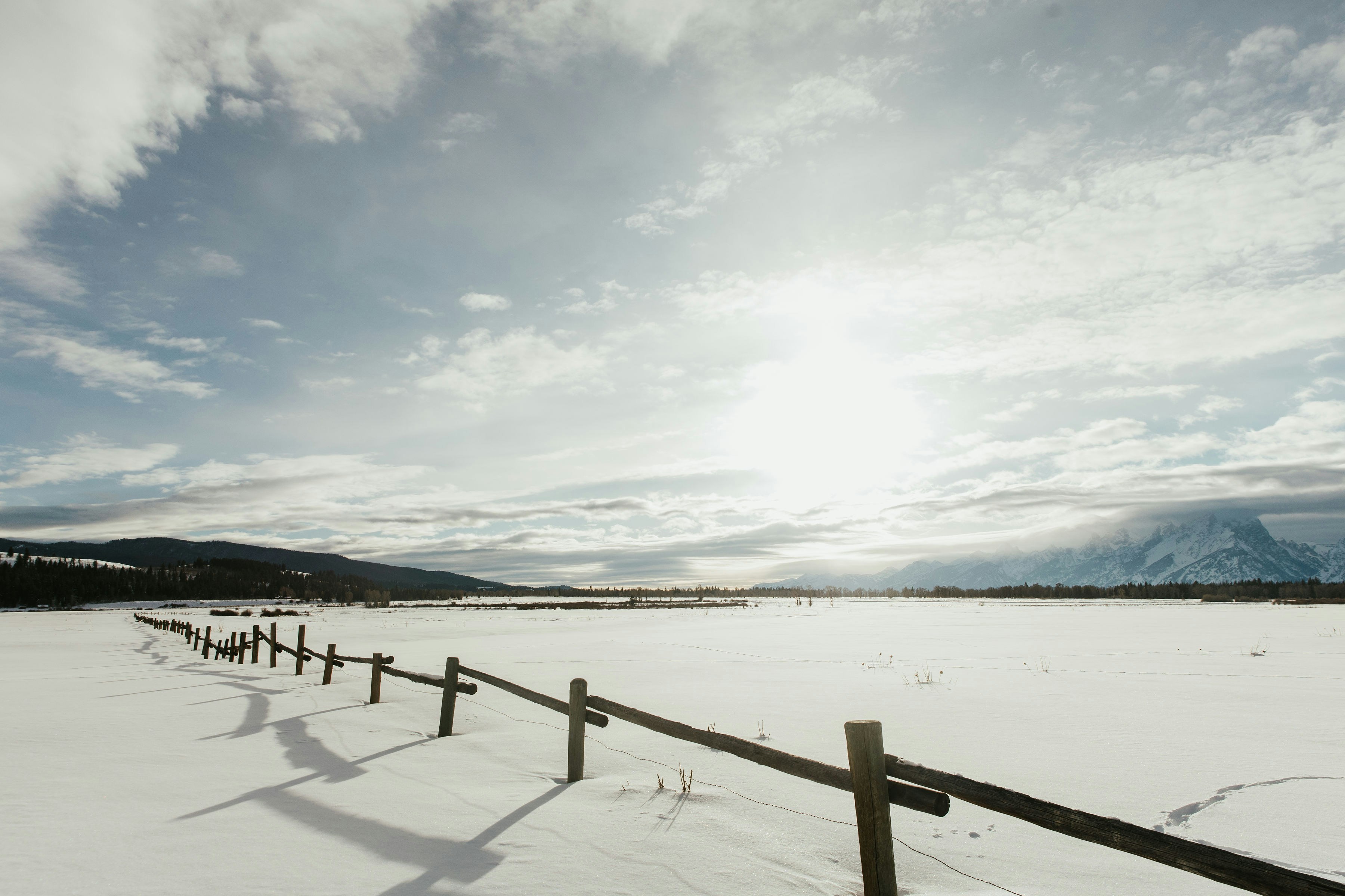 A snow covered field with a fence and mountains in the background