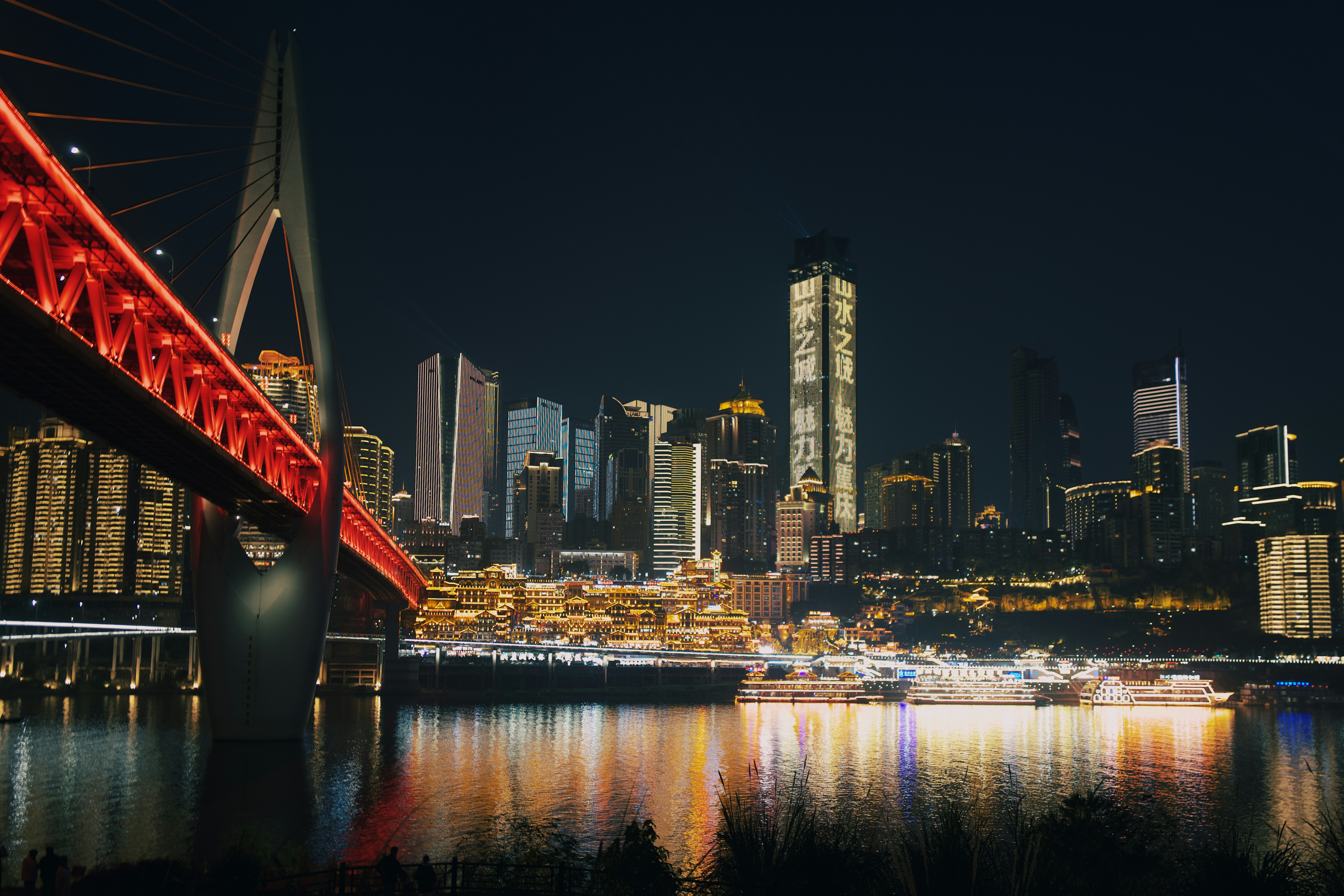 A red bridge over a body of water with a city in the background