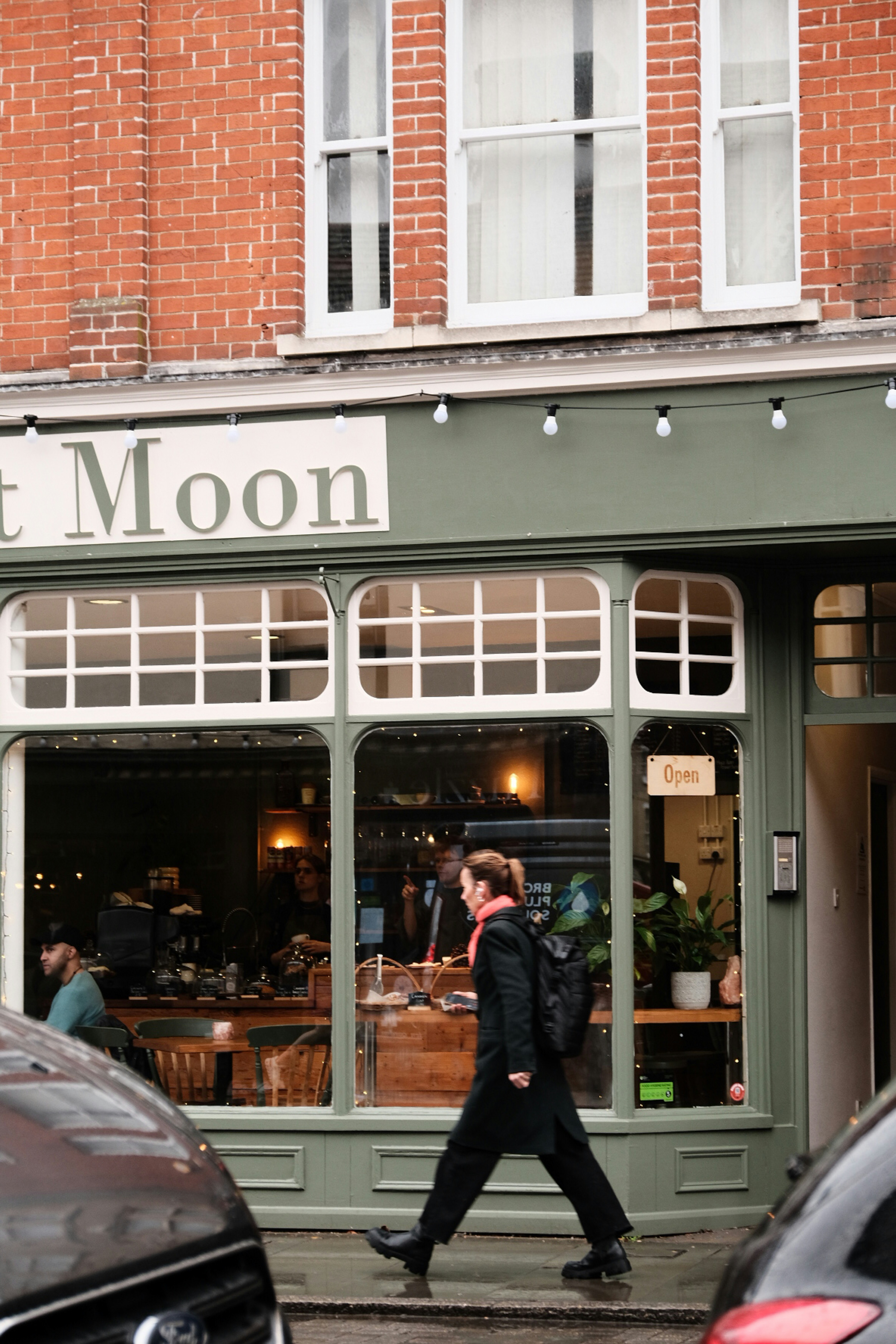 A man walking past a store front with cars parked in front of it