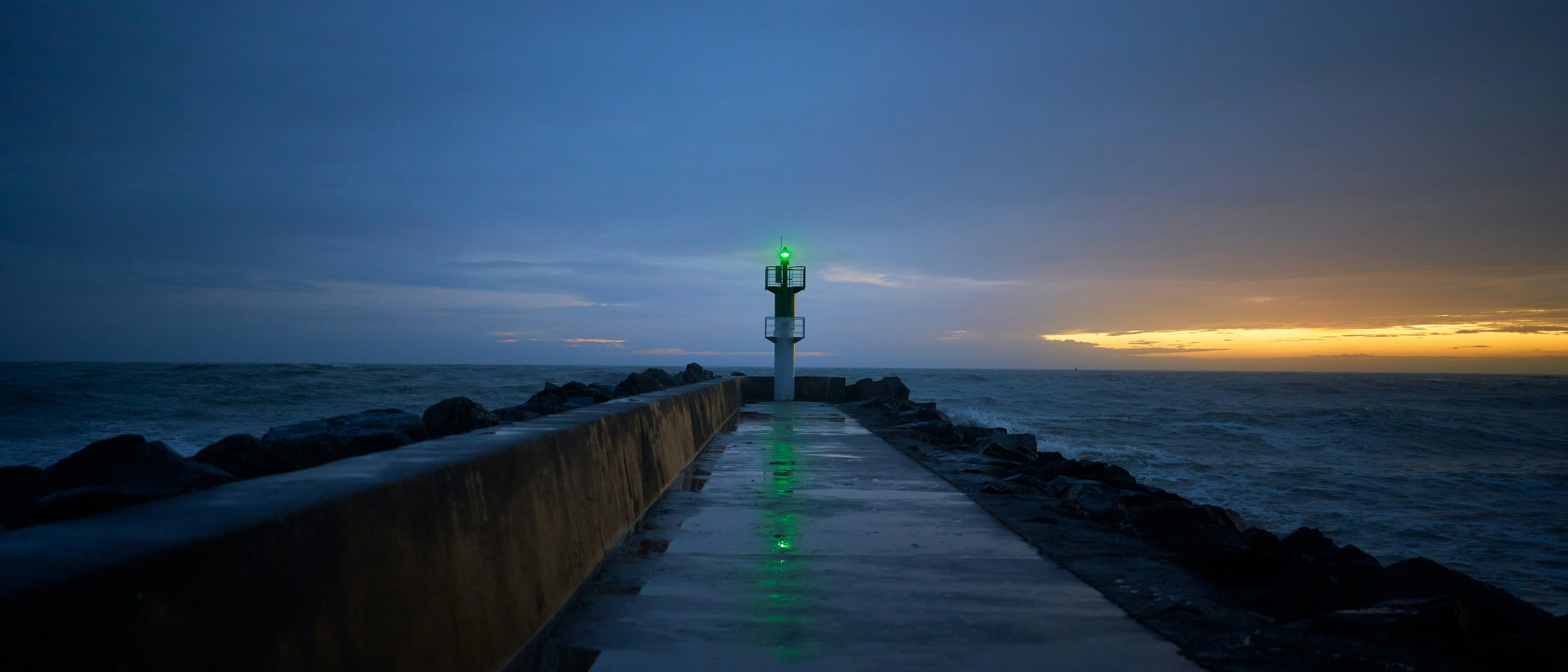 A long pier with a green light at the end of it