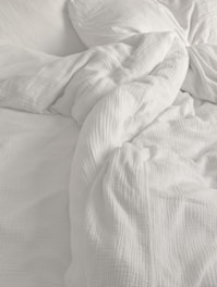 An unmade bed with white sheets and pillows