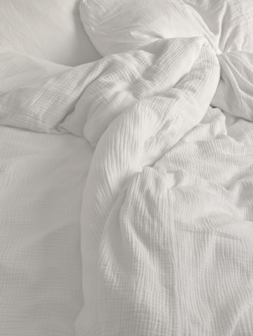 An unmade bed with white sheets and pillows
