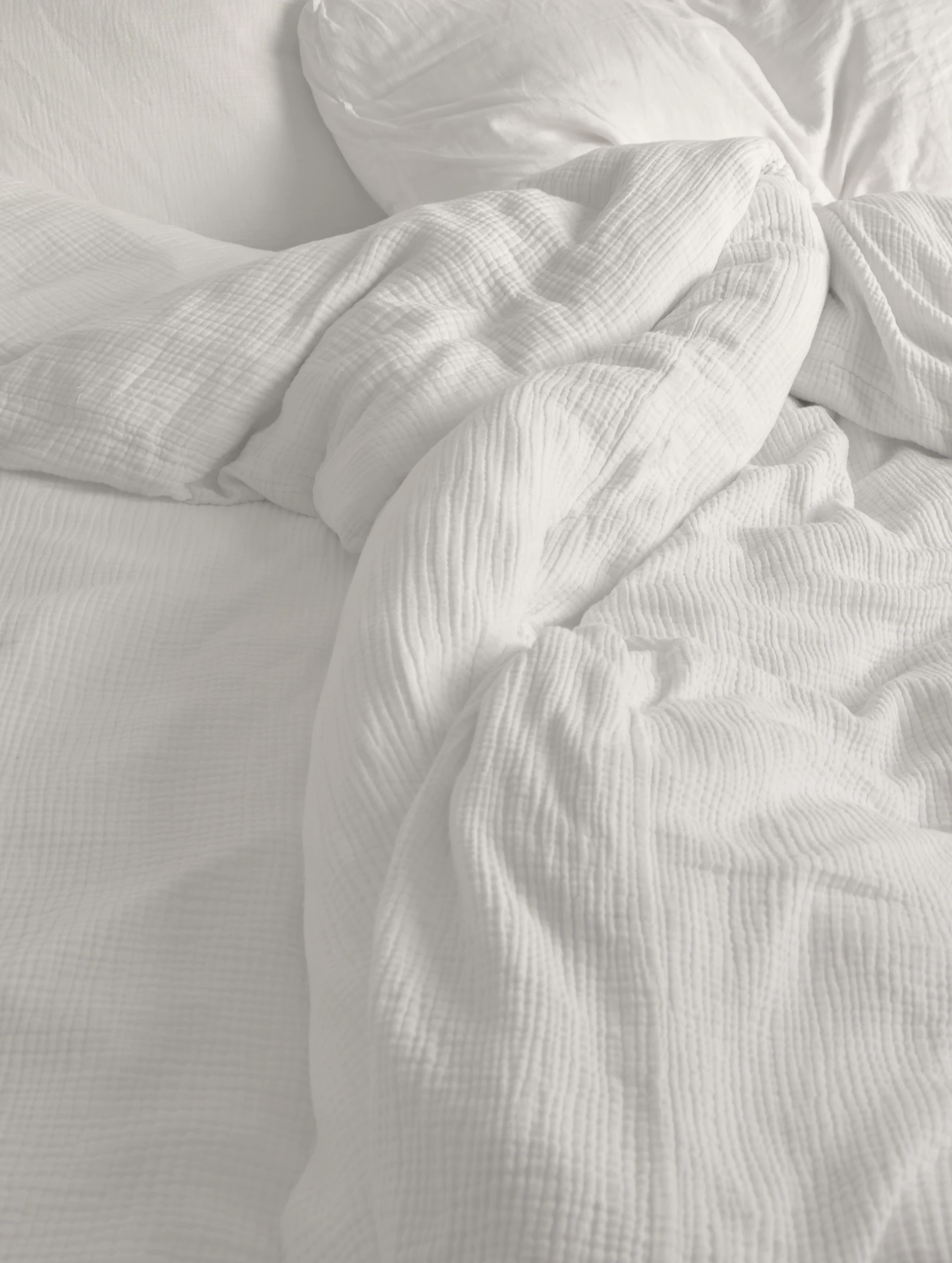 An unmade bed with white sheets and pillows