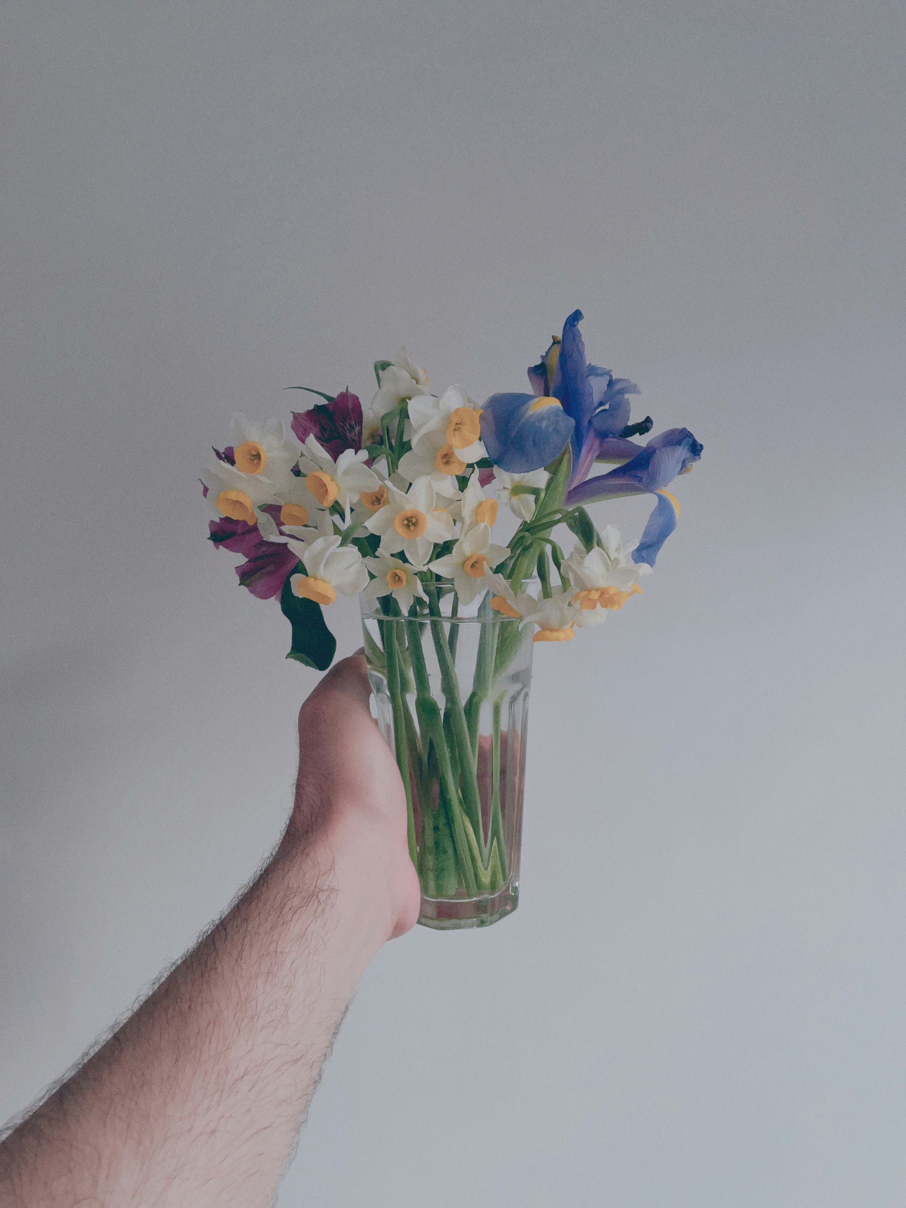 A hand holding a vase with flowers in it