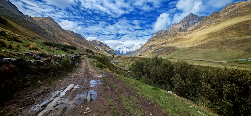 A dirt road surrounded by mountains under a cloudy blue sky