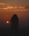 A silhouette of a woman standing in front of a sunset