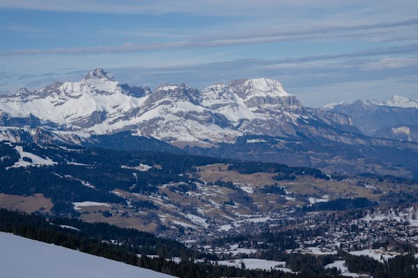 The snow-covered Aravis mountain chain across the valley, with village rooftops and wooded hills below