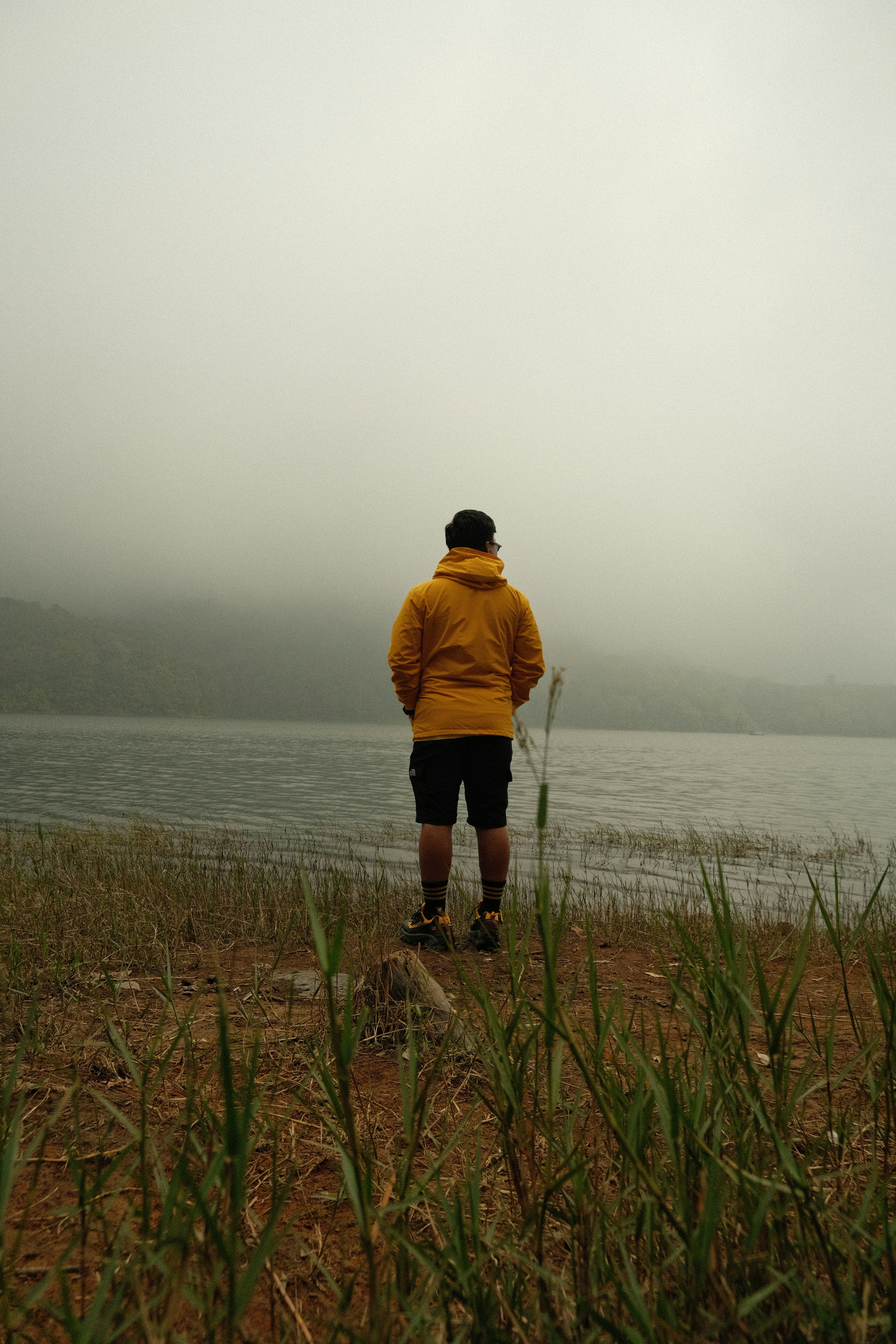 A man in a yellow jacket is standing by the water