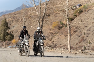 Two people riding motorcycles down a dirt road