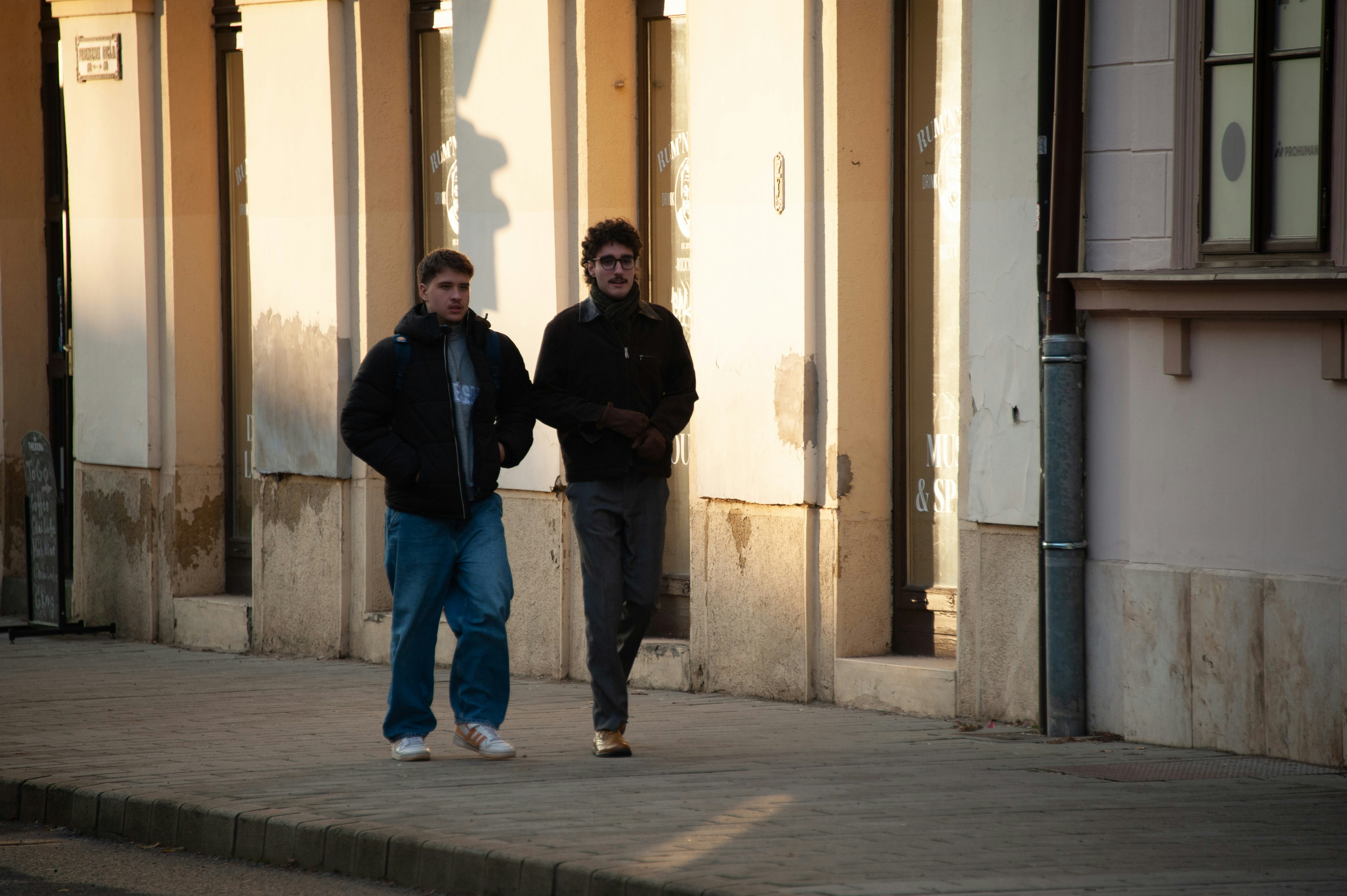 Two men walking down a sidewalk in front of a building photo – Free ...