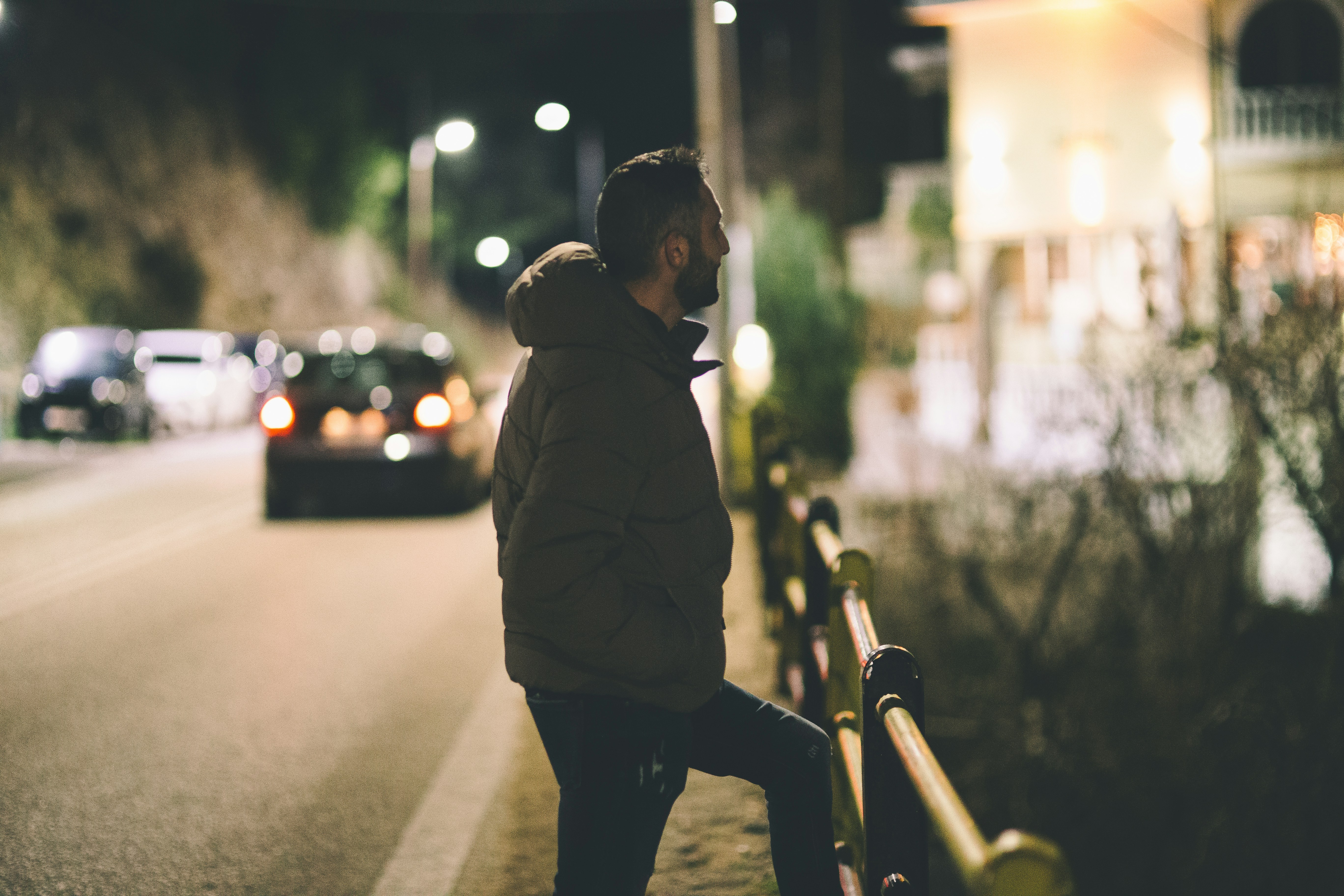 A person leaning against a fence on a street at night