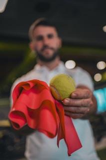 A man holding a tennis ball and a red ribbon