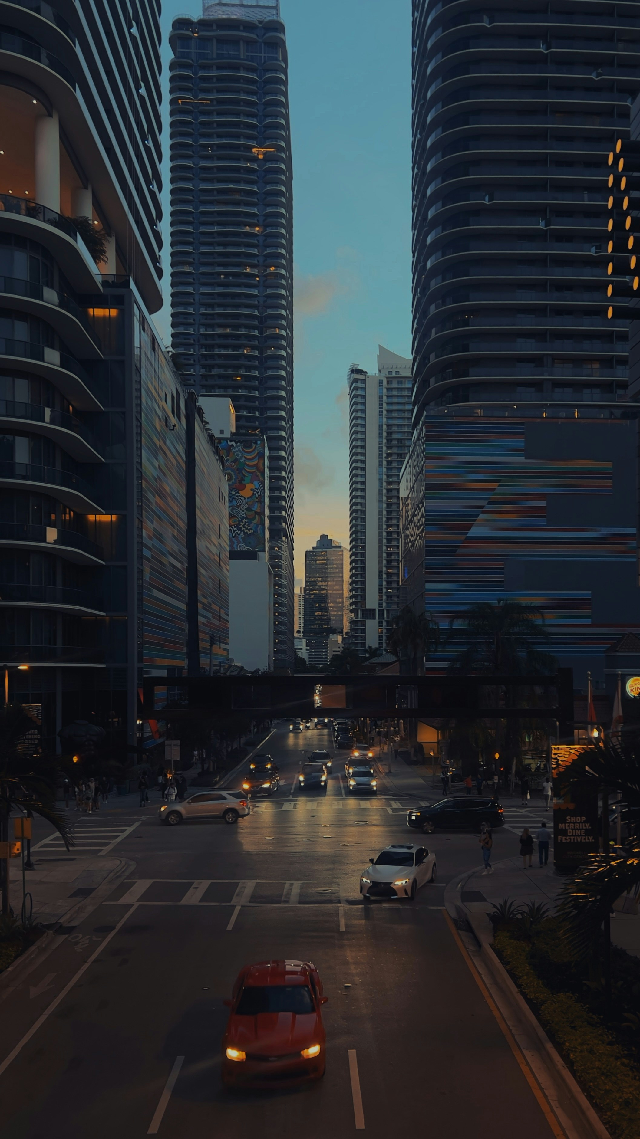 A red car driving down a street next to tall buildings