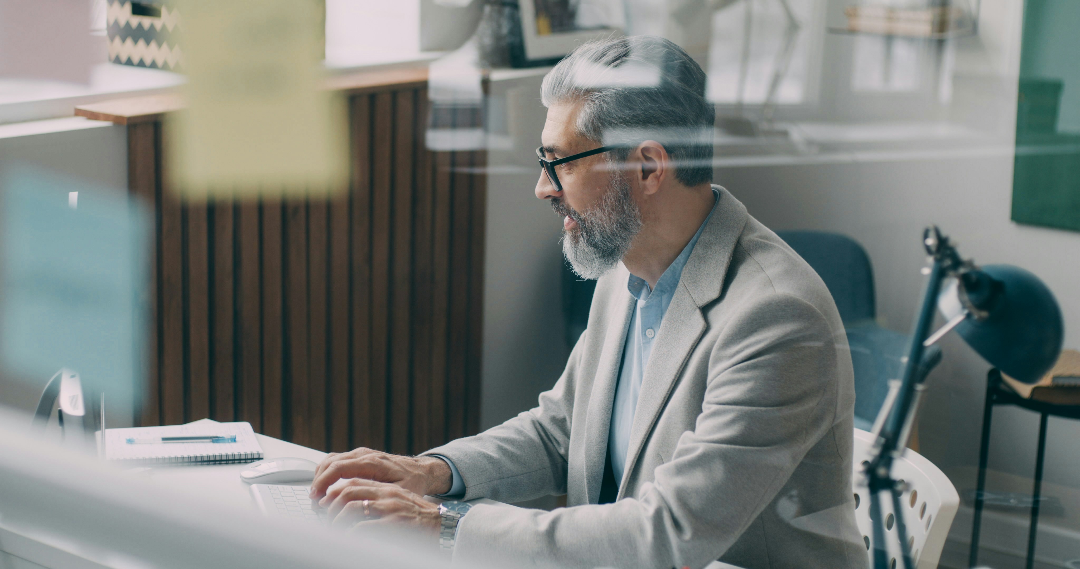 A real estate broker's desk with two monitors: one showing a crowded email inbox and CRM, the other showing a clean dashboard where an AI agent is auto-responding to queries.
